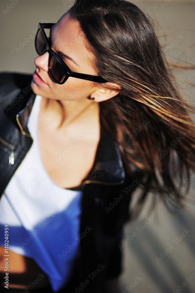 Young beautiful brunette girl in white shirt and leather jacket sunbathing near the water. Wearing sunglasses. Outside. hair blowing in the wind Young beautiful brunette girl in white shirt and leather jacket sunbathing near the water. Wearing sunglasses. Outside. hair blowing in the wind