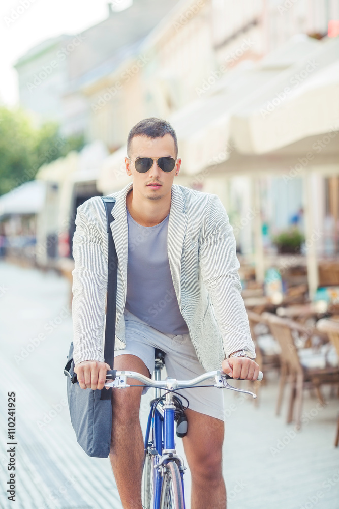 Portrait of a handsome young businessman riding a bicycle. He is traveling to work by bicycle through the downtown in the summer morning.