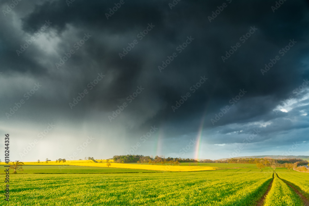 Dark Rainy Clouds and a Rainbow over British Spring Farm Land Dark Rainy Clouds and a Rainbow over British Spring Farm Land