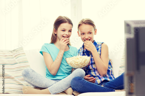 happy girls with popcorn watching tv at home