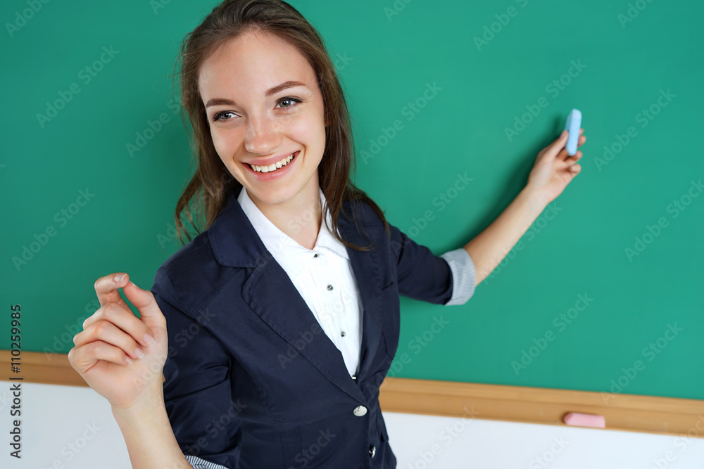 Smiling student or teacher standing in front of the blank blackboard with piece of chalk in her hand. Education concept Smiling student or teacher standing in front of the blank blackboard with piece of chalk in her hand. Education concept