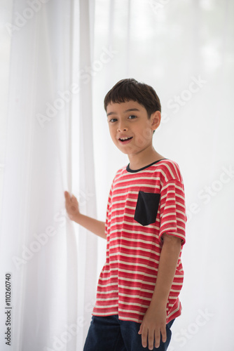 Little boy opening the white curtain