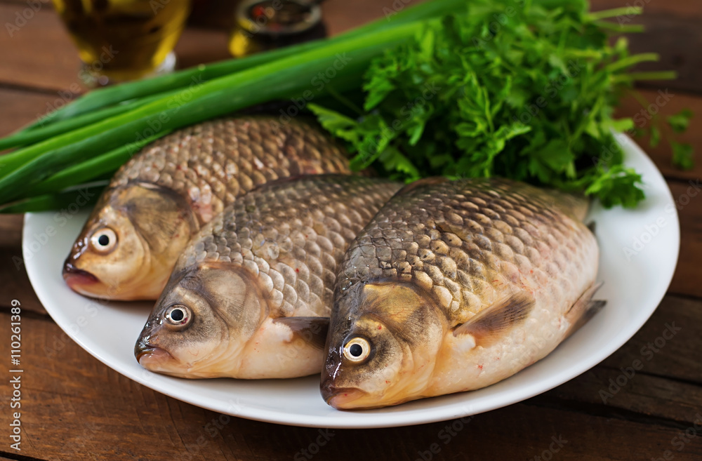 Three fresh raw crucian on a wooden background with herbs Three fresh raw crucian on a wooden background with herbs