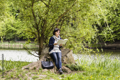 woman reading a book in a park near the lake