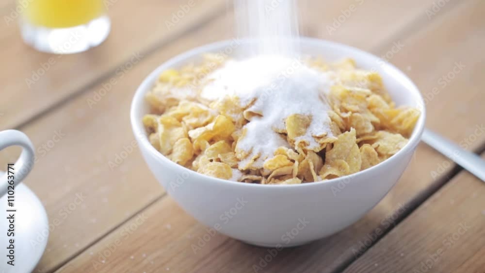 sugar pouring to corn flakes on wooden table sugar pouring to corn flakes on wooden table