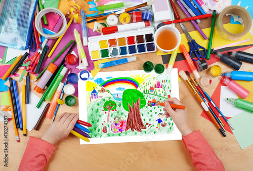 people relax on meadow near the village , child drawing, top view hands with pencil painting picture on paper, artwork workplace