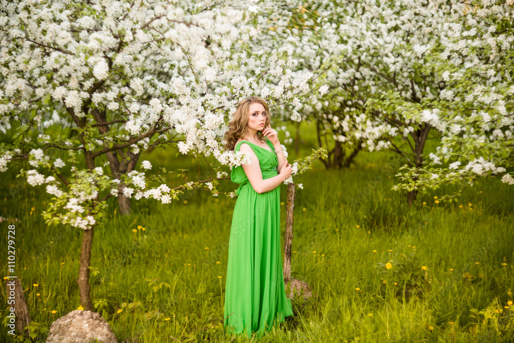 beautiful young blond woman standing beside a blossoming Apple tree