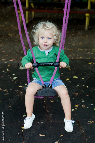 Funny blond boy riding on a swing