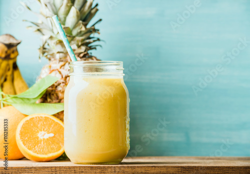 Freshly blended yellow and orange fruit smoothie in glass jar with straw
