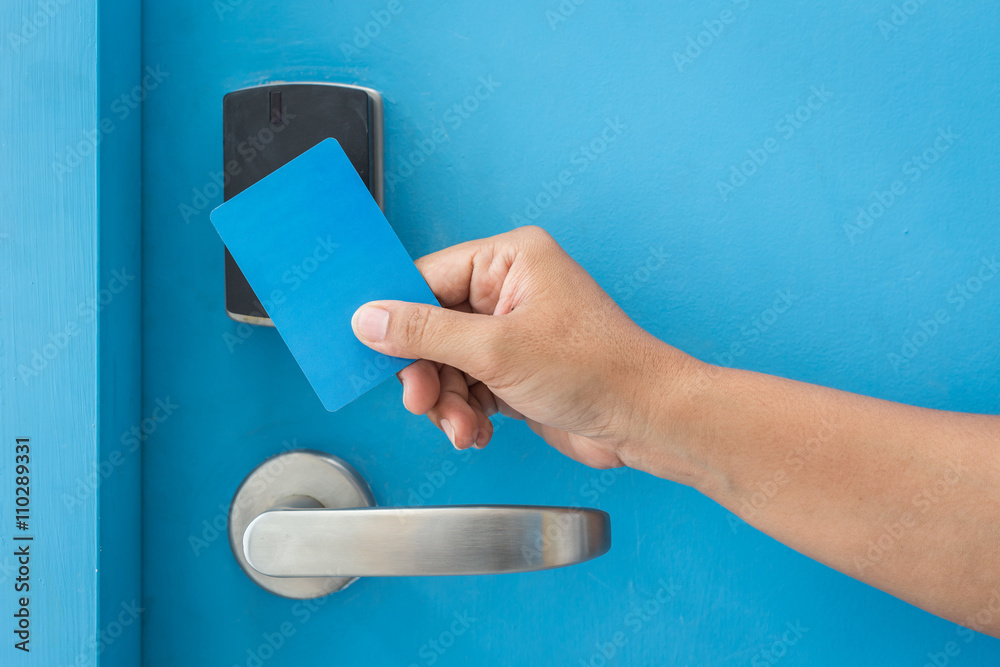 Fototapeta premium Hand holding blue hotel keycard in front of electric door