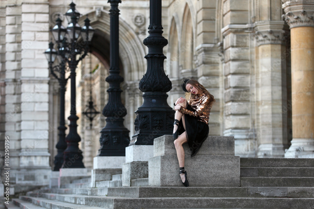 Sad ballerina in black skirt, haze and golden top sitting in front of a palace