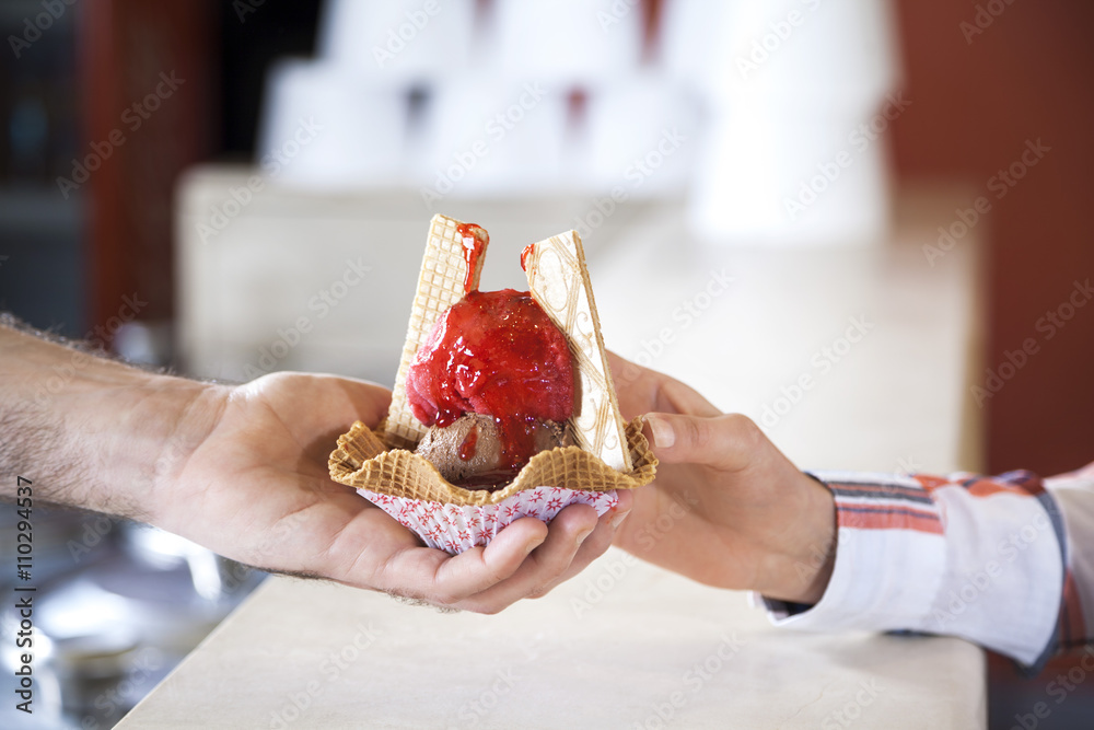 Waiter's Hand Giving Ice Cream With Strawberry Syrup To Woman