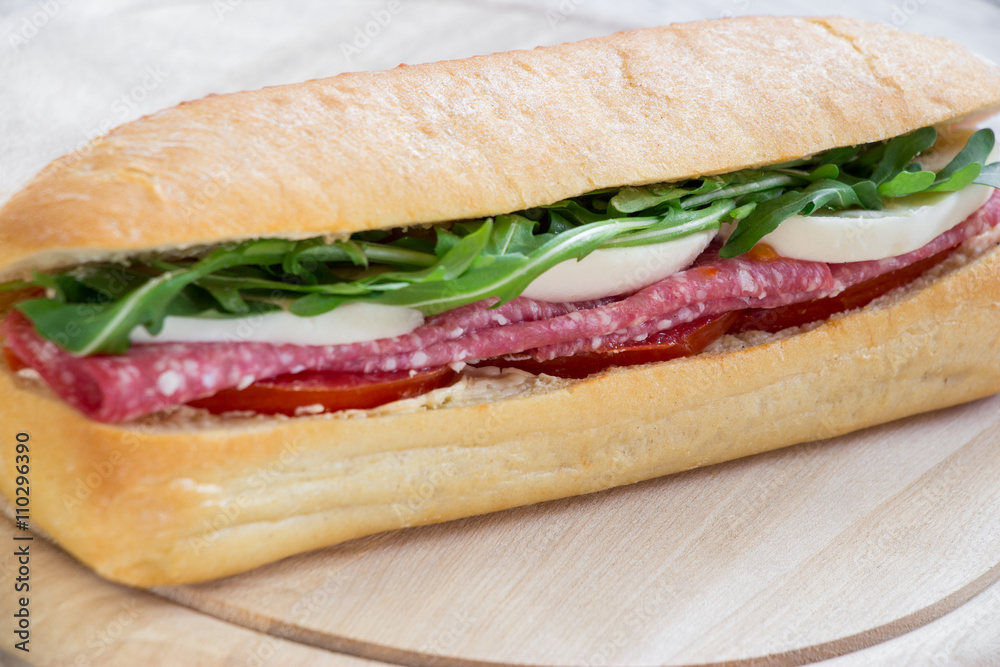 Sandwich with salami, mozzarella, arugula and tomatoes.