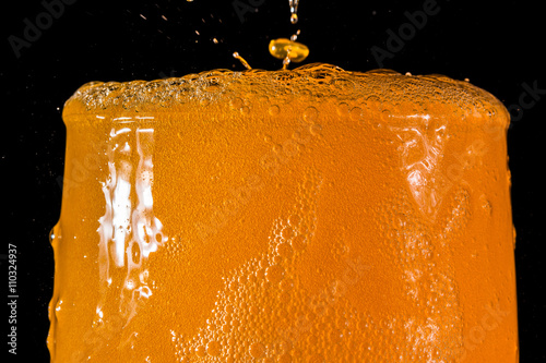 Orange soda large glass, overflowing glass of orange soda closeup with bubbles isolated on black background
