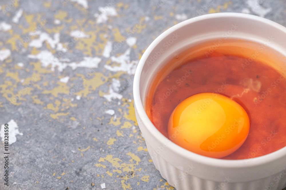 Raw eggs with tomatoes in the ramekins on the stone table Raw eggs with tomatoes in the ramekins on the stone table