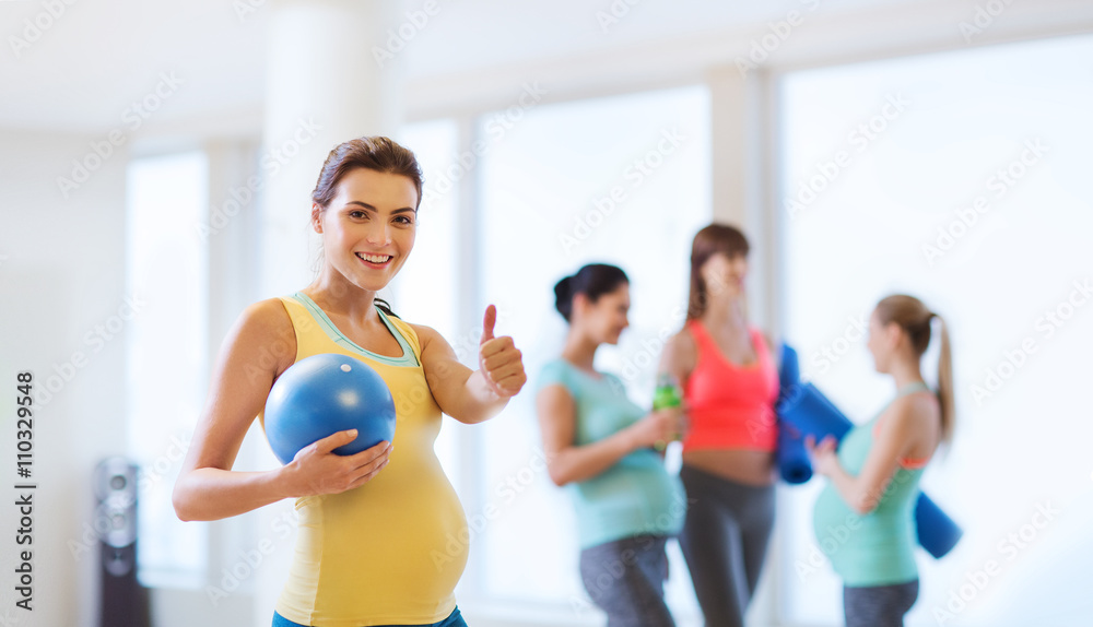 pregnant woman with ball in gym showing thumbs up 