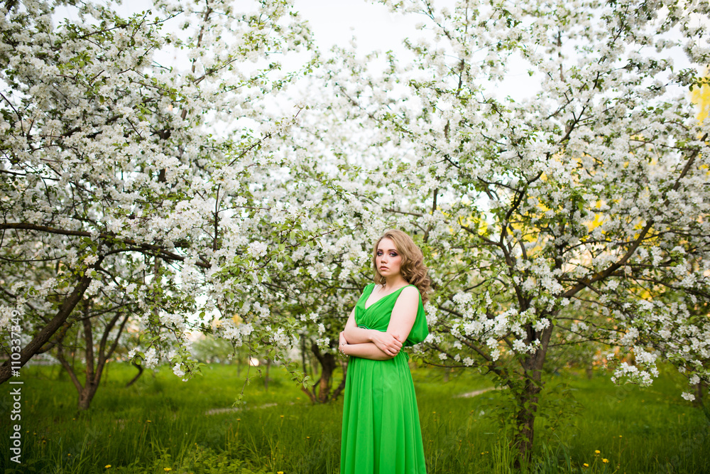 beautiful young blond woman standing beside a blossoming Apple tree