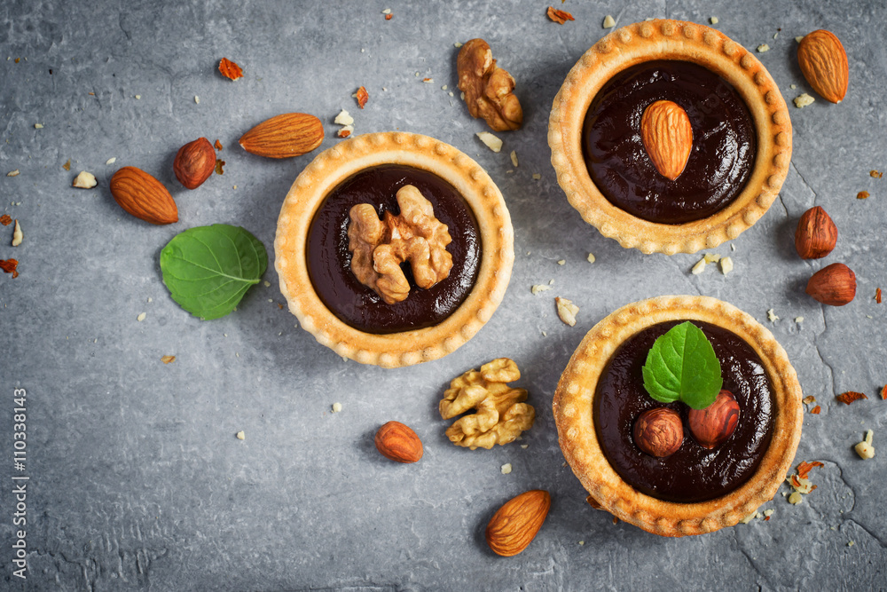Small Chocolate Tarts decorated with different nuts on a gray st Small Chocolate Tarts decorated with different nuts on a gray st