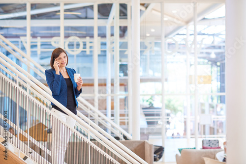 Businesswoman standing on stairs in bright office space with pho