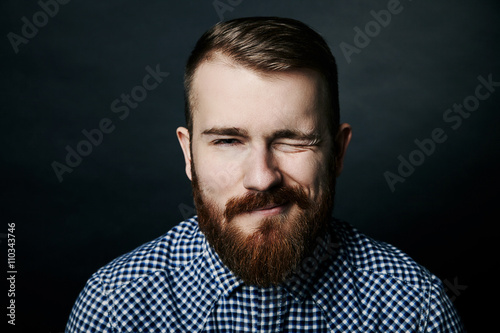 Winking red bearded man studio portrait on dark background © julenochek