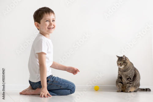 the boy plays on a floor with a cat with a yellow ball