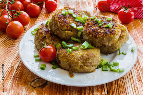 Roasted chicken cutlets with green onion on white plate and small cherry tomatoes on wooden background. 