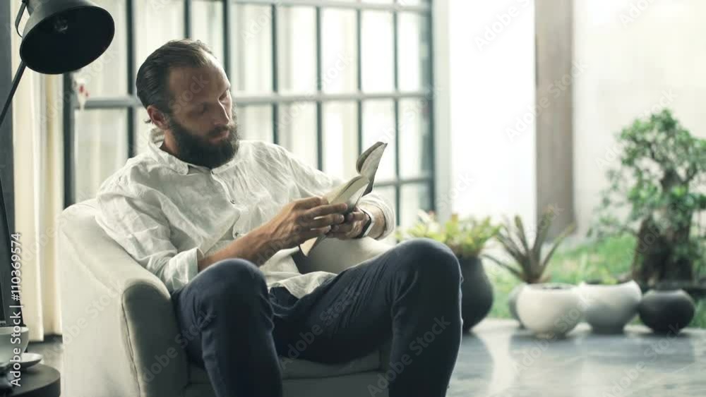 Young man reading book armchair in living room at home
Young man reading book armchair in living room at home