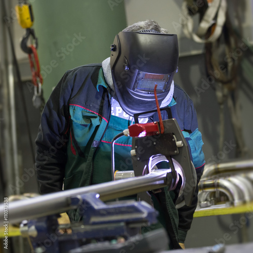 Fotografie Industrial operator setting  computer controlled process of orbital welding machine in inox pipes manufacturing workshop