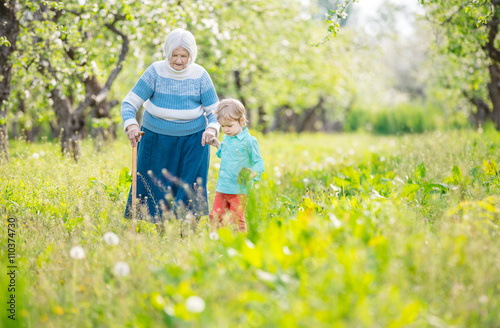 Senior woman supported by great grandson walking in blossoming orchard 