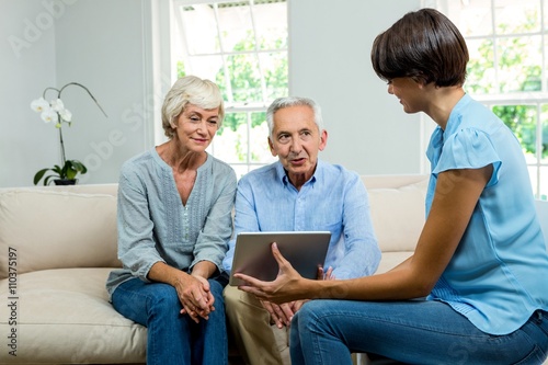 Female consultant showing digital tablet to aged couple at home