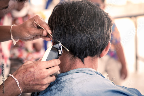 Old man having a haircut with a hair clippers in barber shop
