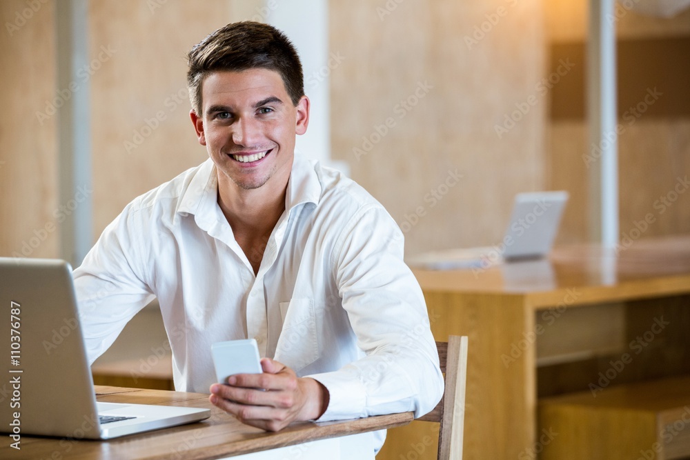 Portrait of man holding mobile phone and laptop on a desk Portrait of man holding mobile phone and laptop on a desk