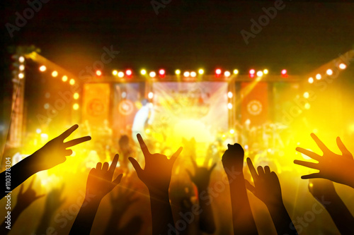 Audience with hands raised at a music festival and lights streaming down from above the stage. live concert, music festival, happy youth, luxury party, landscape exterior.
