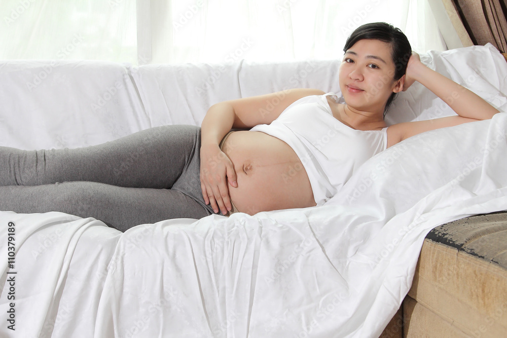 Beautiful asian woman pregnant resting on the sofa in the home with lighting of sunlight Beautiful asian woman pregnant resting on the sofa in the home with lighting of sunlight