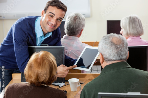 Smiling Teacher Showing Digital Tablet To Senior Students In Cla