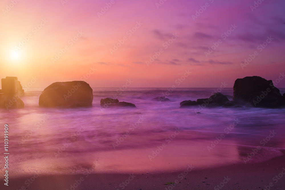 Summer seasonal natural vacation background. Romantic morning at sea. Big boulders sticking out from smooth wavy sea. Pink horizon with first hot sun rays. Long exposure. 