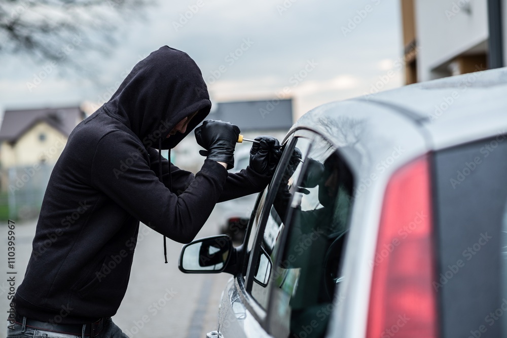 Car thief trying to break into a car with a screwdriver.