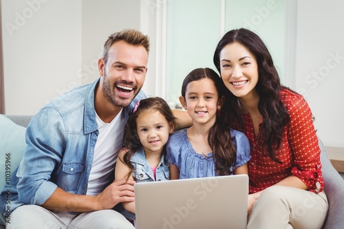 Portrait of family smiling and using laptop on sofa