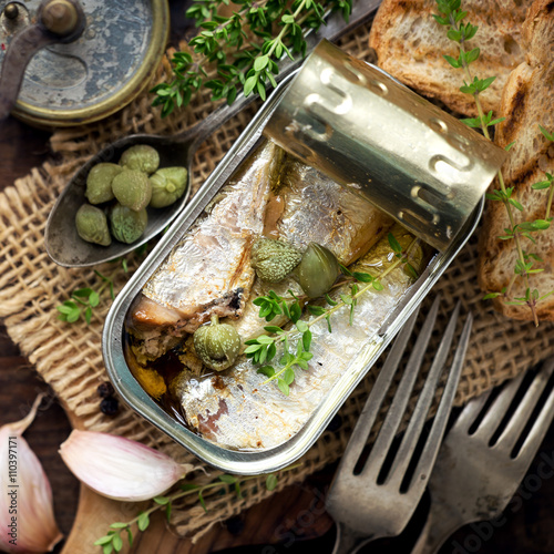 Quadro em tela Open tin of sardines in olive oil with capers and thyme on dark rustic wooden ba