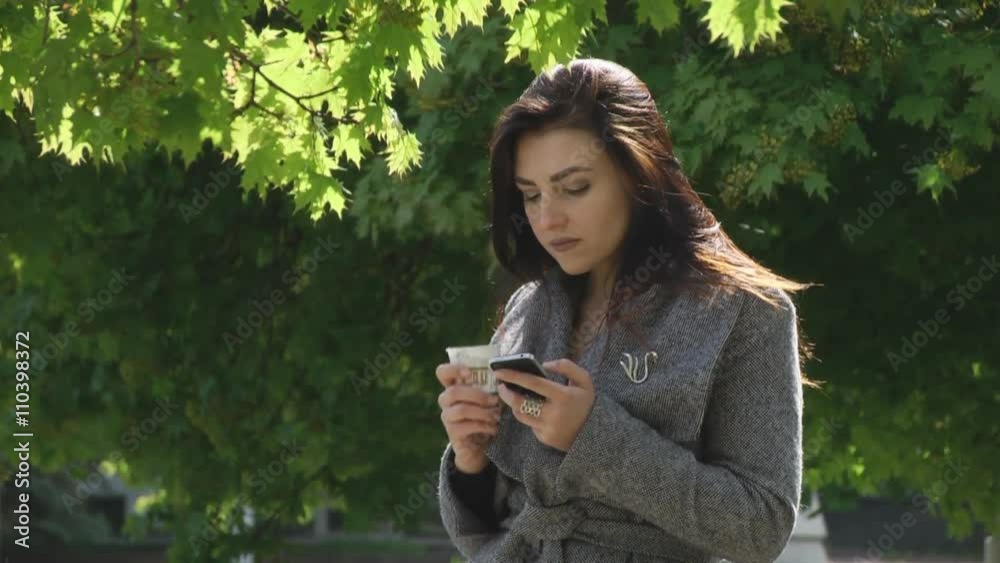 SheThe girl in a park drinking coffee and looking to the smartphone. Then he distracted, as if something she saw, smiled and went back to the phone hands the phone coffee SheThe girl in a park drinking coffee and looking to the smartphone. Then he distracted, as if something she saw, smiled and went back to the phone hands the phone coffee