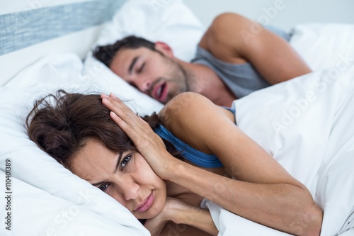 Woman blocking ears with hands while man snoring on bed photo