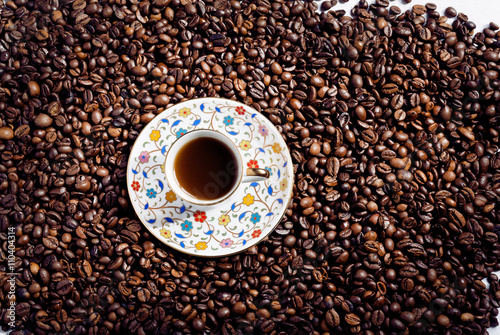 Bright mass of arabica coffee beans and small plate with coffee cup in oriental style. Top view on coffee.