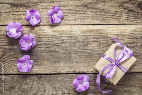 Gift box with ribbon, purple flowers on wood background with emp