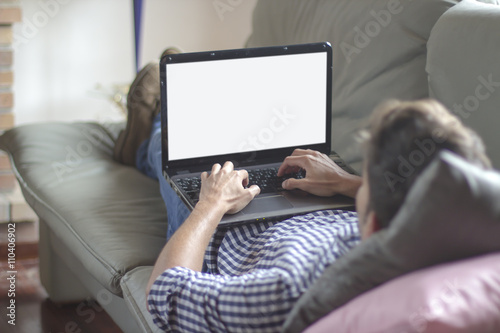 Young man lying comfortably on the sofa while using the laptop w