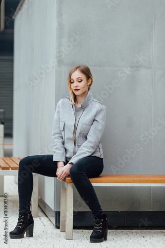 Young woman sitting on the bench in front of buindings photo