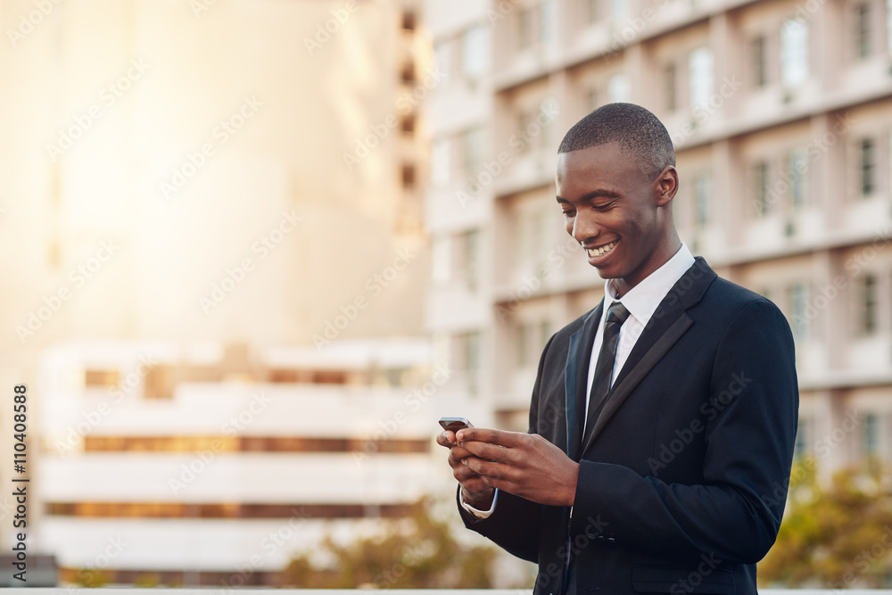 Young African entrepreneur smiling at his phone in a city Young African entrepreneur smiling at his phone in a city