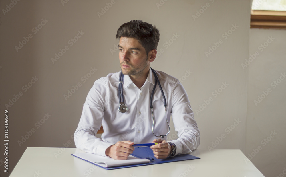 Frontal view of a young doctor looking to the side. He is sittin Frontal view of a young doctor looking to the side. He is sittin