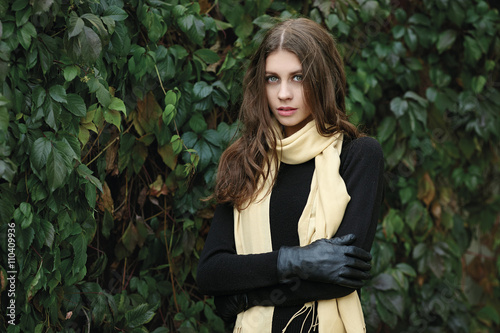 Outdoor portrait of young beautiful brunette woman with wavy long hair stares into camera posing against ivy wall background