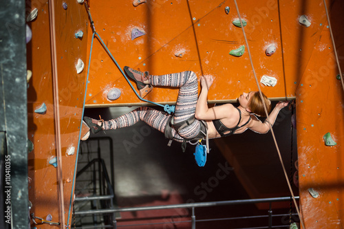 Strong woman with special equipment climbs on an indoor rock-climbing wall