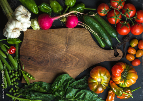 Fresh raw ingredients for healthy cooking or salad making with dark wooden cutting baoard in center, top view, copy space photo